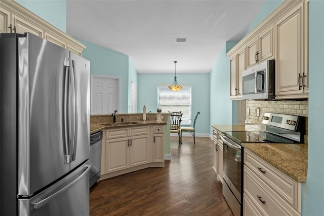 kitchen featuring a peninsula, a sink, stainless steel appliances, cream cabinetry, and backsplash