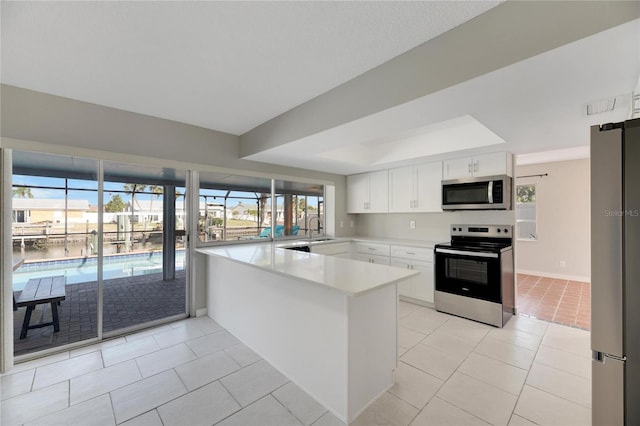 kitchen featuring a raised ceiling, appliances with stainless steel finishes, kitchen peninsula, white cabinets, and light tile patterned flooring