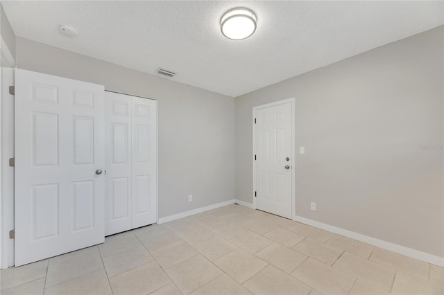 unfurnished bedroom featuring a textured ceiling, a closet, and light tile patterned floors