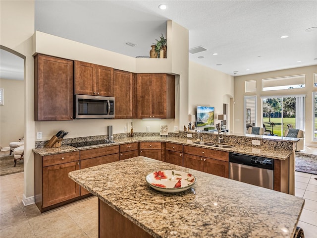 kitchen with kitchen peninsula, appliances with stainless steel finishes, light stone countertops, sink, and light tile patterned floors