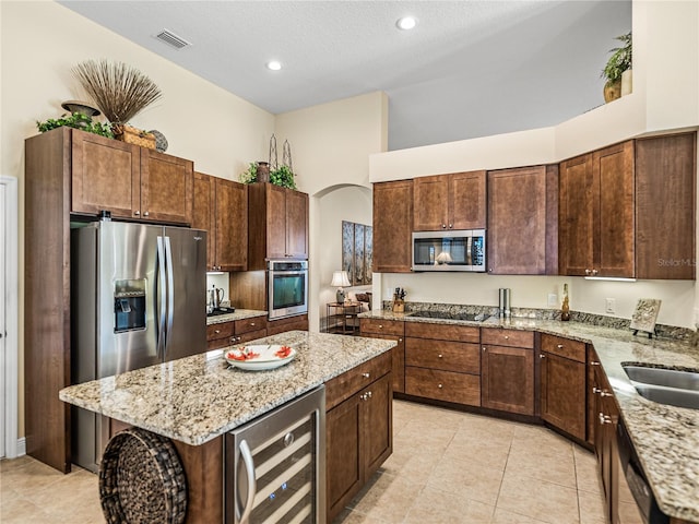 kitchen with a high ceiling, wine cooler, light stone countertops, a kitchen island, and stainless steel appliances