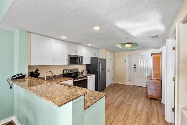 kitchen featuring kitchen peninsula, appliances with stainless steel finishes, white cabinetry, and dark stone countertops