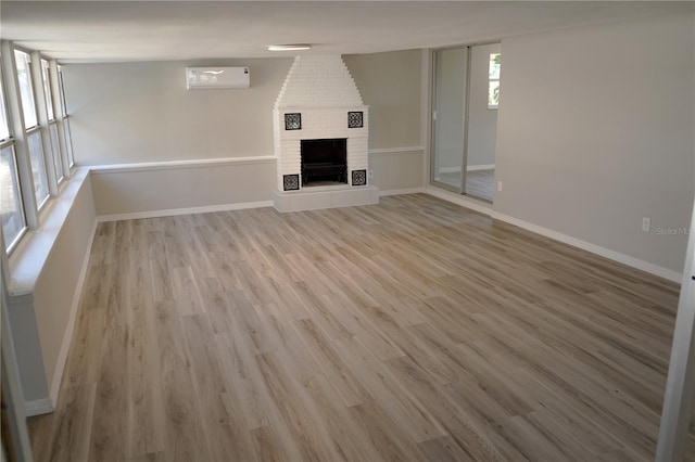 unfurnished living room with light wood-type flooring, a fireplace, and a wall mounted AC