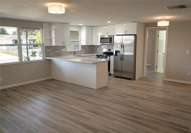 kitchen featuring white cabinets, sink, light hardwood / wood-style floors, kitchen peninsula, and stainless steel appliances