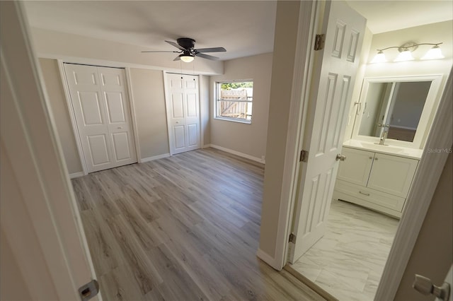 unfurnished bedroom with two closets, connected bathroom, light hardwood / wood-style floors, and ceiling fan