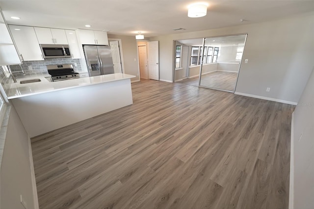 kitchen featuring white cabinetry, tasteful backsplash, light hardwood / wood-style flooring, kitchen peninsula, and appliances with stainless steel finishes