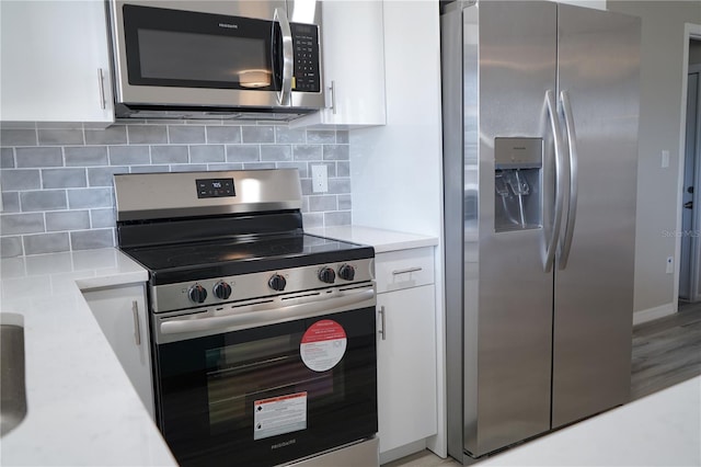 kitchen with white cabinets, appliances with stainless steel finishes, backsplash, and light hardwood / wood-style flooring