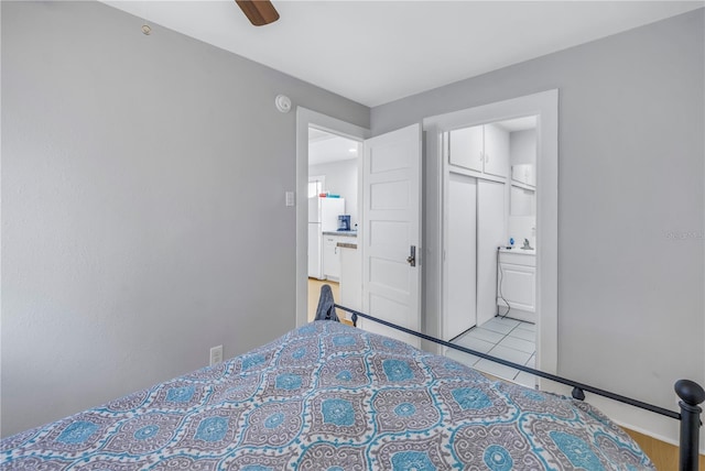 bedroom with a closet, ensuite bath, ceiling fan, and white fridge