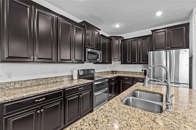 kitchen featuring light stone counters, sink, a textured ceiling, and appliances with stainless steel finishes