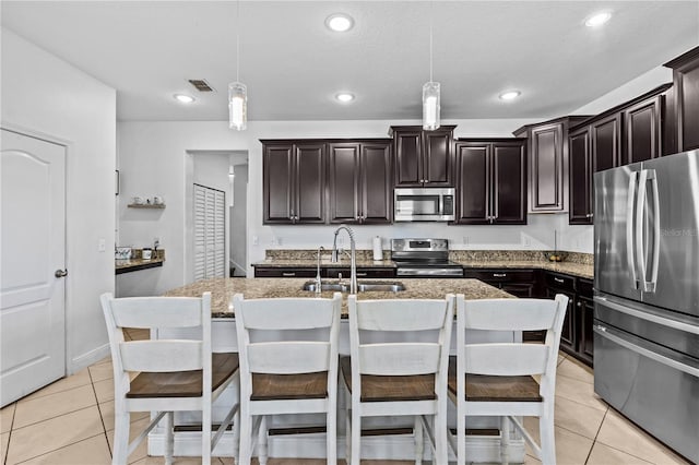 kitchen with dark brown cabinets, stainless steel appliances, a kitchen island with sink, sink, and pendant lighting