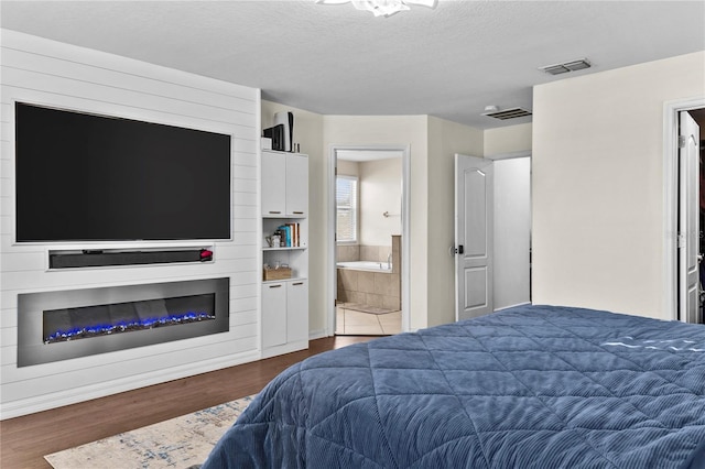 bedroom with a textured ceiling, ensuite bathroom, a fireplace, and dark hardwood / wood-style floors