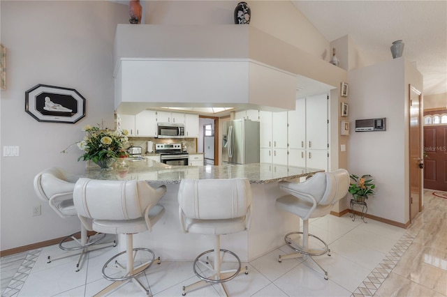 kitchen featuring white cabinetry, light stone countertops, kitchen peninsula, light tile patterned flooring, and appliances with stainless steel finishes