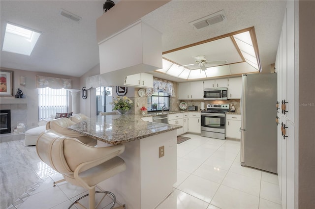 kitchen featuring white cabinetry, stone counters, ceiling fan, kitchen peninsula, and appliances with stainless steel finishes