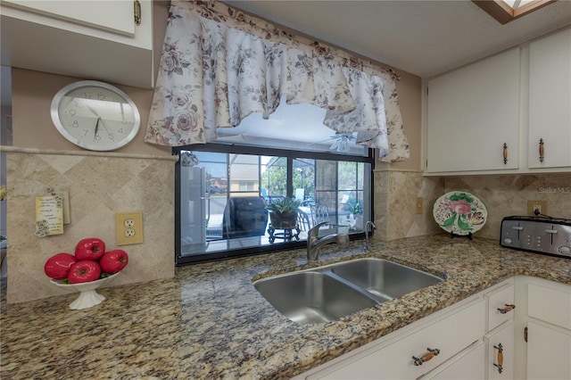 kitchen with tasteful backsplash, light stone countertops, sink, and white cabinets