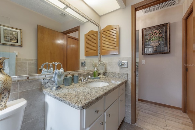 bathroom featuring tile patterned flooring, vanity, toilet, and tile walls