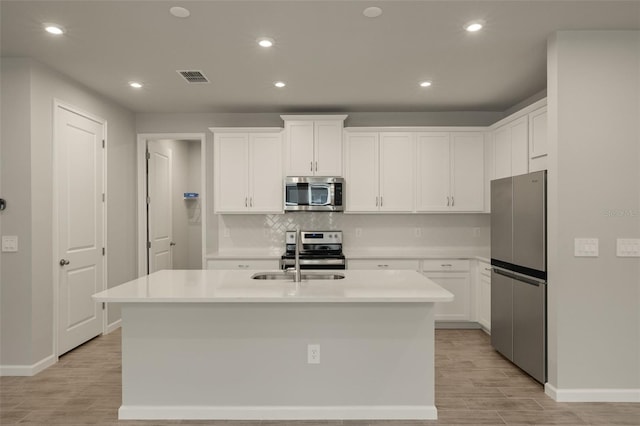 kitchen with sink, white cabinetry, a center island with sink, stainless steel appliances, and backsplash