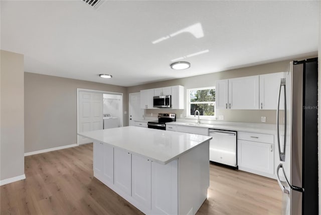 kitchen featuring appliances with stainless steel finishes, light wood-type flooring, a kitchen island, sink, and white cabinetry