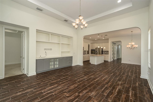 unfurnished living room featuring dark hardwood / wood-style floors, a raised ceiling, and an inviting chandelier