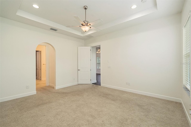 carpeted spare room featuring a tray ceiling and ceiling fan