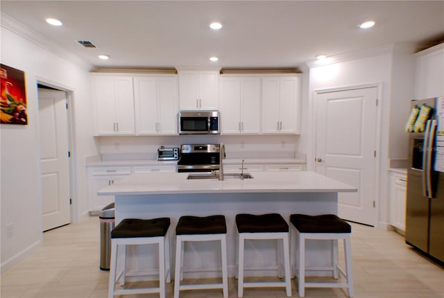 kitchen featuring appliances with stainless steel finishes, white cabinetry, a kitchen island with sink, and sink