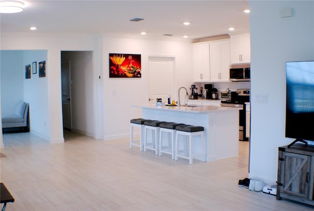 kitchen featuring a kitchen breakfast bar, stainless steel appliances, sink, a center island with sink, and white cabinets