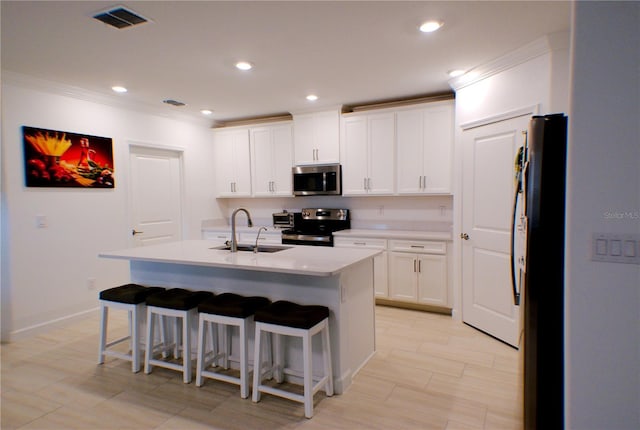 kitchen with a breakfast bar, stainless steel appliances, sink, white cabinets, and an island with sink