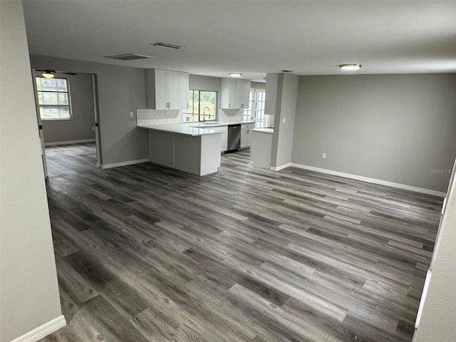 kitchen with kitchen peninsula, dark wood-type flooring, stainless steel dishwasher, and a healthy amount of sunlight