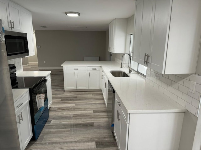 kitchen featuring kitchen peninsula, light wood-type flooring, stainless steel appliances, sink, and white cabinets