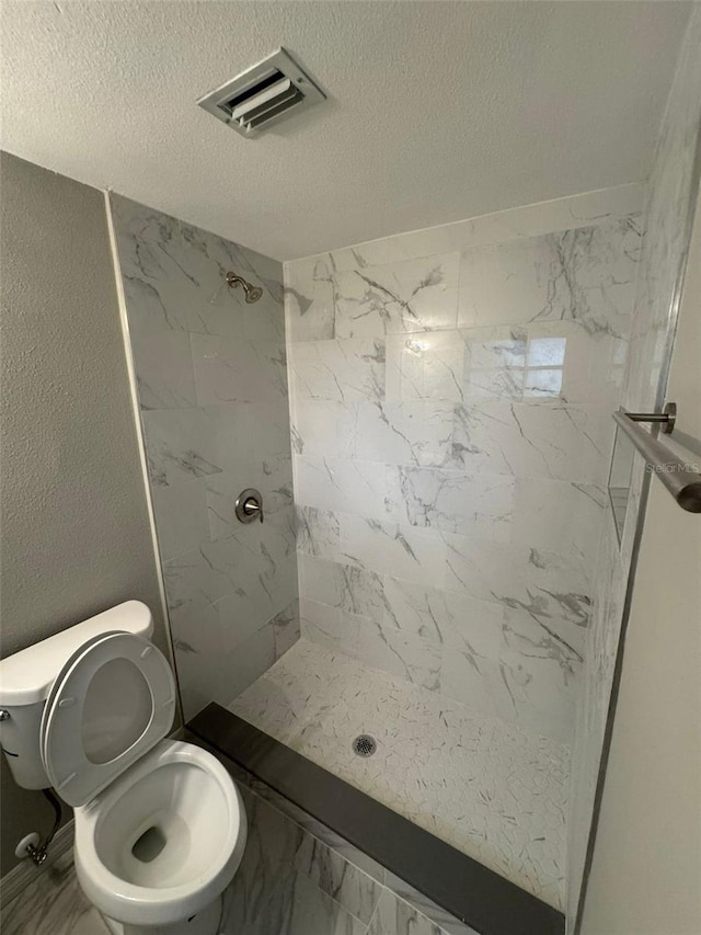 bathroom featuring toilet, a textured ceiling, and a tile shower