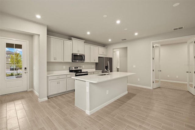 kitchen featuring stainless steel appliances, an island with sink, sink, and white cabinets