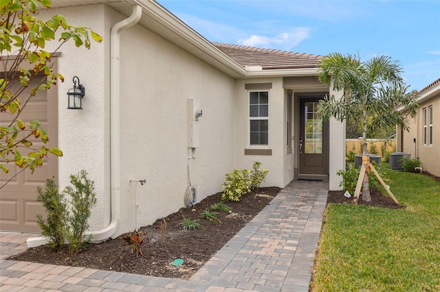 entrance to property featuring cooling unit, a yard, and a garage