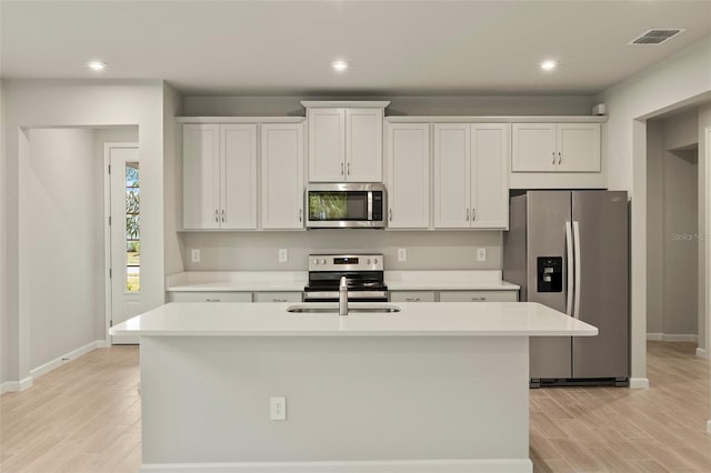 kitchen with an island with sink, sink, white cabinets, light hardwood / wood-style floors, and stainless steel appliances