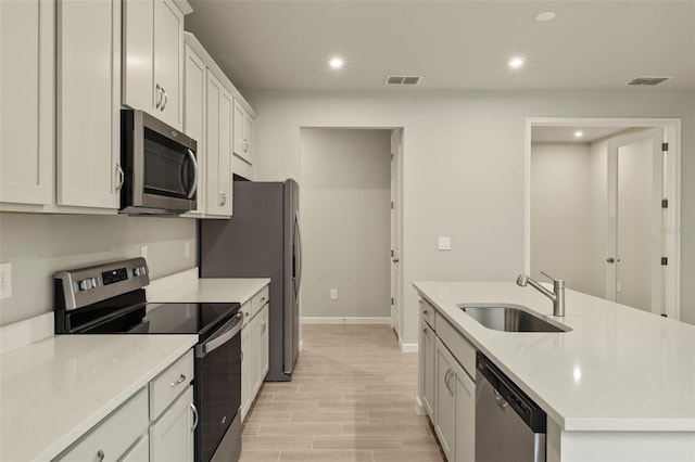 kitchen with sink, appliances with stainless steel finishes, light hardwood / wood-style floors, an island with sink, and white cabinets