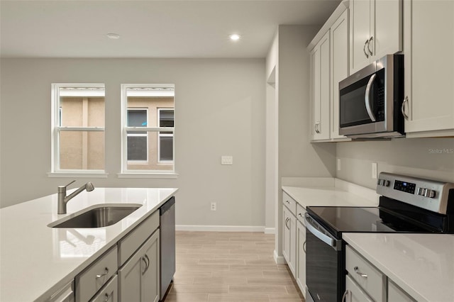 kitchen with light stone counters, sink, light hardwood / wood-style floors, and appliances with stainless steel finishes