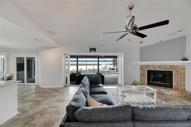 living room with a tiled fireplace, ceiling fan, and lofted ceiling