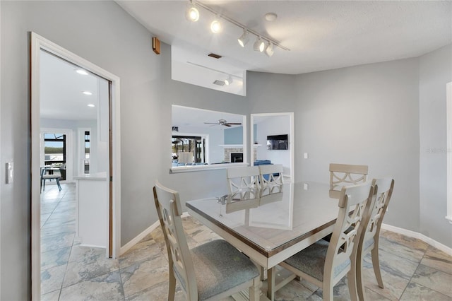 dining area with ceiling fan, a fireplace, rail lighting, and a textured ceiling