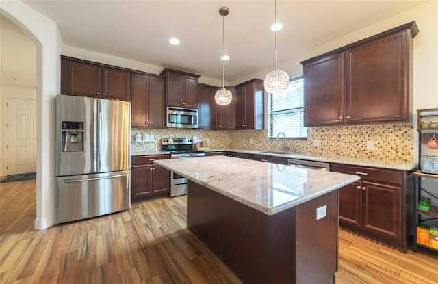 kitchen with a kitchen island, light hardwood / wood-style floors, stainless steel appliances, and hanging light fixtures