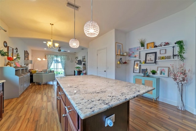 kitchen featuring light stone countertops, a center island, wood-type flooring, decorative light fixtures, and ceiling fan with notable chandelier