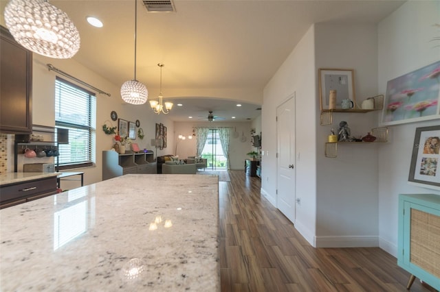 kitchen featuring ceiling fan with notable chandelier, hanging light fixtures, light stone countertops, dark brown cabinets, and dark hardwood / wood-style flooring