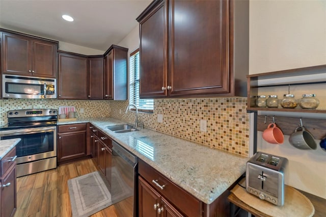 kitchen with backsplash, sink, light hardwood / wood-style flooring, light stone countertops, and stainless steel appliances