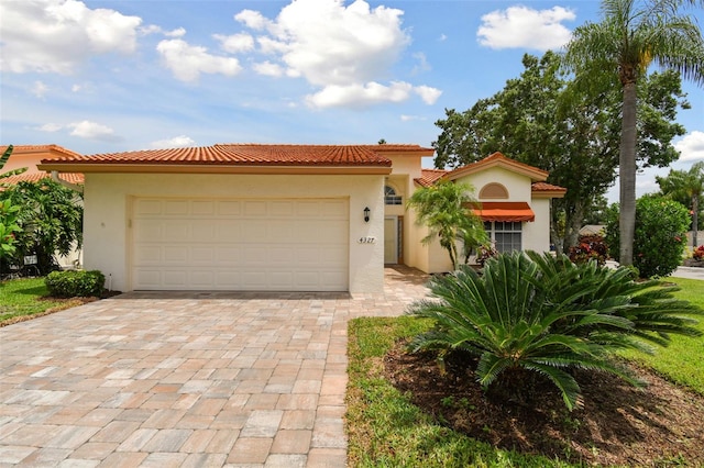 mediterranean / spanish house with a garage, a tiled roof, decorative driveway, and stucco siding