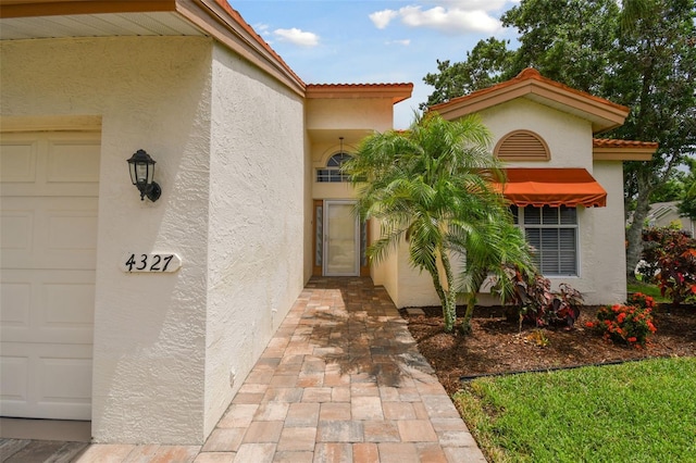 view of exterior entry with a garage, a tiled roof, and stucco siding