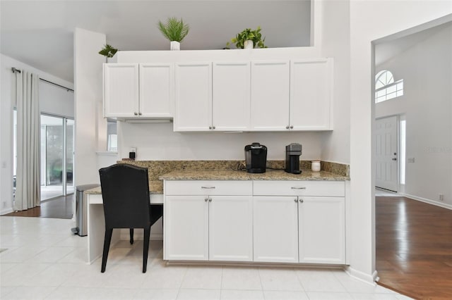 kitchen with a towering ceiling, baseboards, white cabinetry, and light stone counters