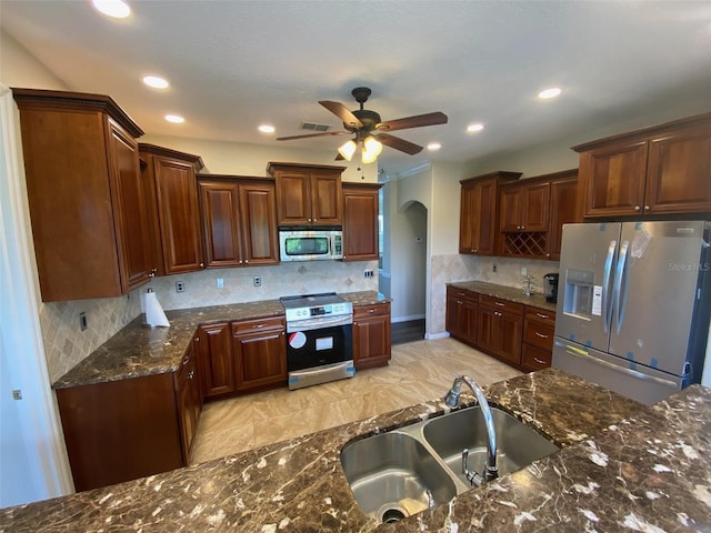 kitchen featuring tasteful backsplash, stainless steel appliances, ceiling fan, sink, and dark stone countertops