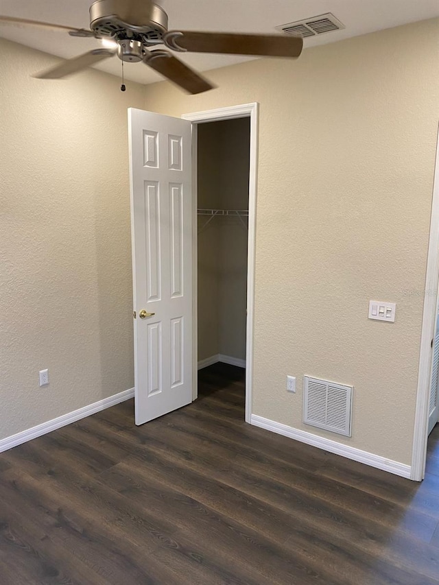 unfurnished bedroom featuring ceiling fan, a spacious closet, dark wood-type flooring, and a closet