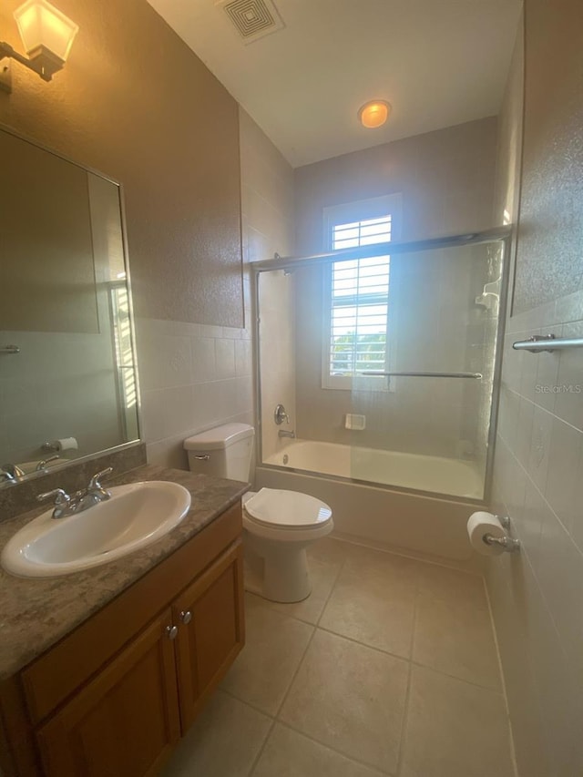 full bathroom featuring tile patterned floors, toilet, shower / bath combination with glass door, vanity, and tile walls