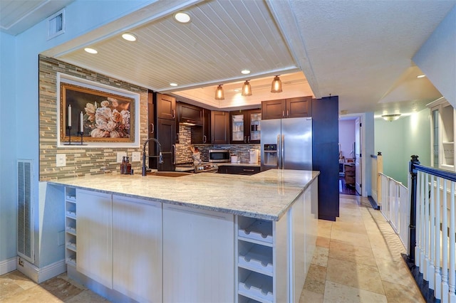 kitchen with light stone counters, kitchen peninsula, backsplash, and appliances with stainless steel finishes