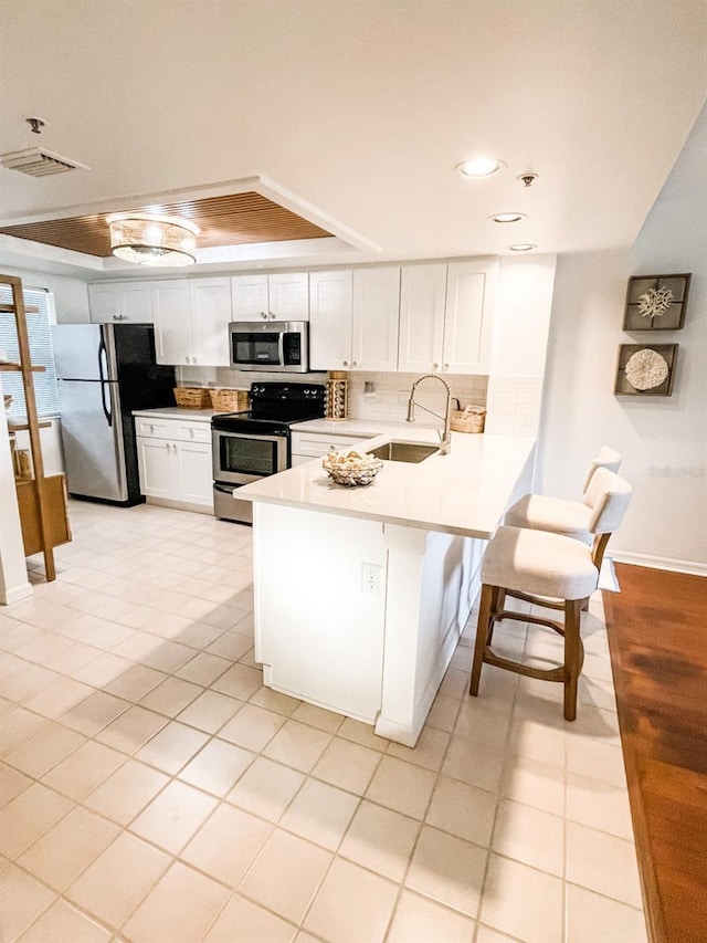 kitchen with white cabinetry, sink, kitchen peninsula, a tray ceiling, and appliances with stainless steel finishes