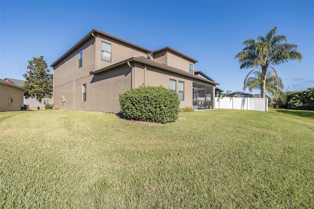 back of house featuring a sunroom, fence, a lawn, and stucco siding