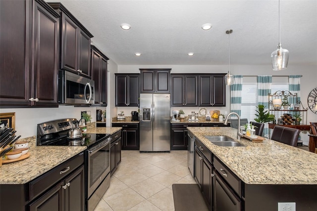 kitchen featuring sink, light tile patterned floors, appliances with stainless steel finishes, a kitchen island with sink, and decorative light fixtures